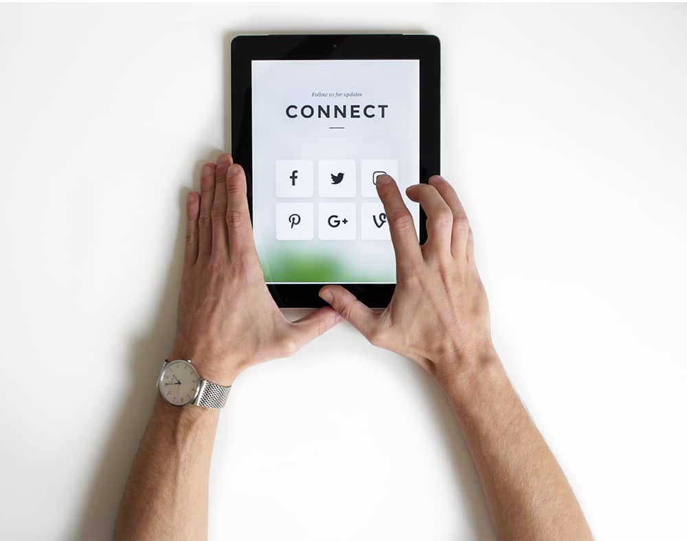 mains d'homme tenant une tablette avec icones réseaux sociaux